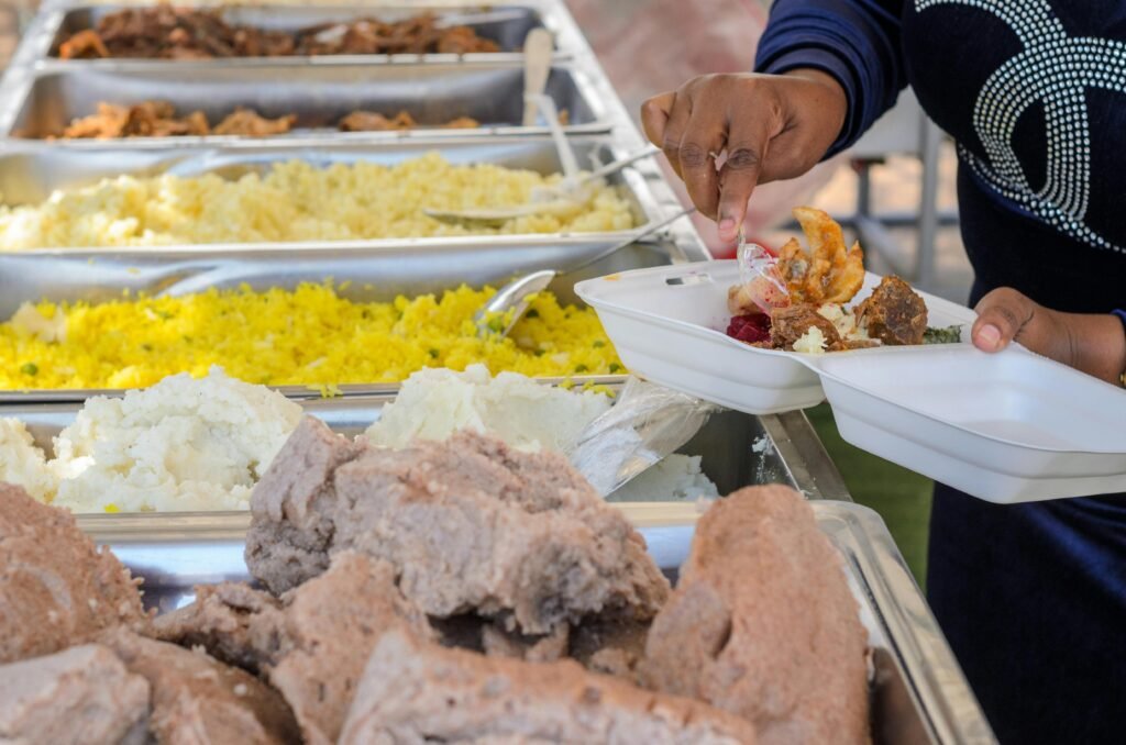 A person serves a variety of foods from a buffet station onto their plate.